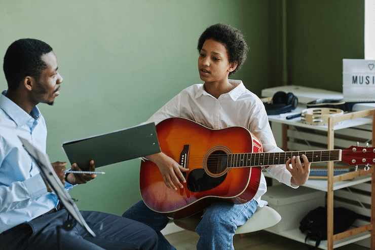 imgi_1_youthful-african-american-schoolgirl-playing-acoustic-guitar-lesson-music-school-while
